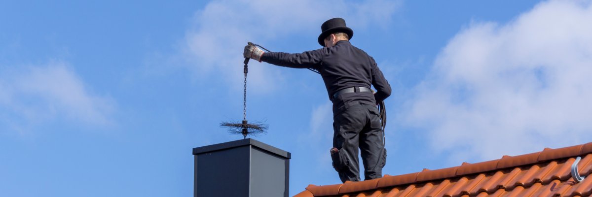 Chimney sweep cleaning a chimney standing on the house roof, lowering equipment down the flue Chimney sweep cleaning a chimney standing on the house roof, lowering equipment down the flue